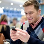 Young man sitting at table in cafe and texting in mobile.